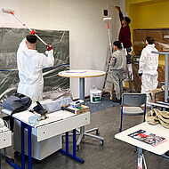 Drei Schüler und ein Malermeister malen ein Klassenzimmer aus.