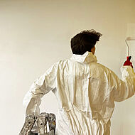 Ein Schüler in einem Maler-Overall streicht eine Wand mit weißer Farbe.