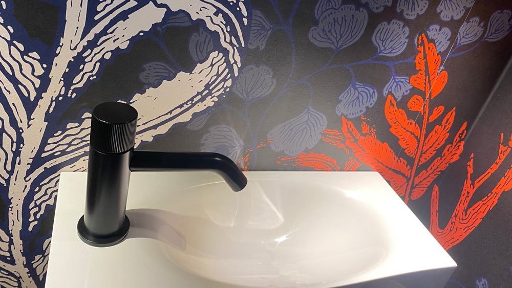 Moderne, Blau-rot-gemusterte Tapete vor einem kleinen Waschbecken in einem WC